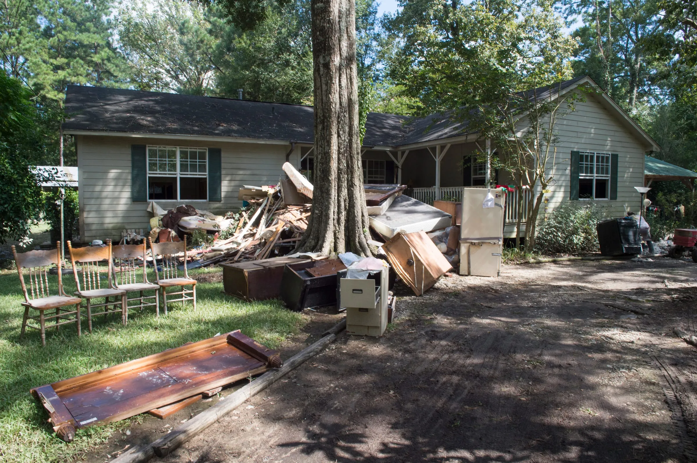 Furniture, appliances and broken lumber piled in front of a house after a flood