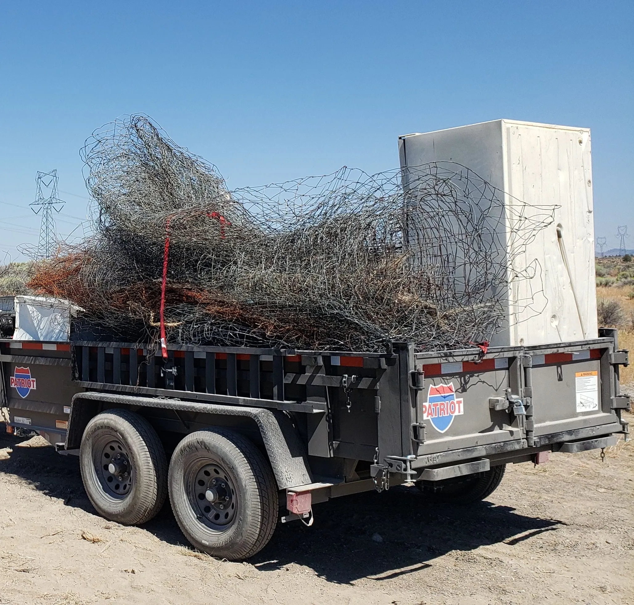 A dump trailer loaded with old wire fencing and a discarded freezer